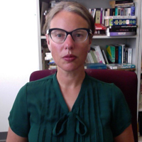 Allison Perlman, in glasses, sits before a bookshelf. 