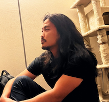a man with long hair sits with his side profile facing the camera