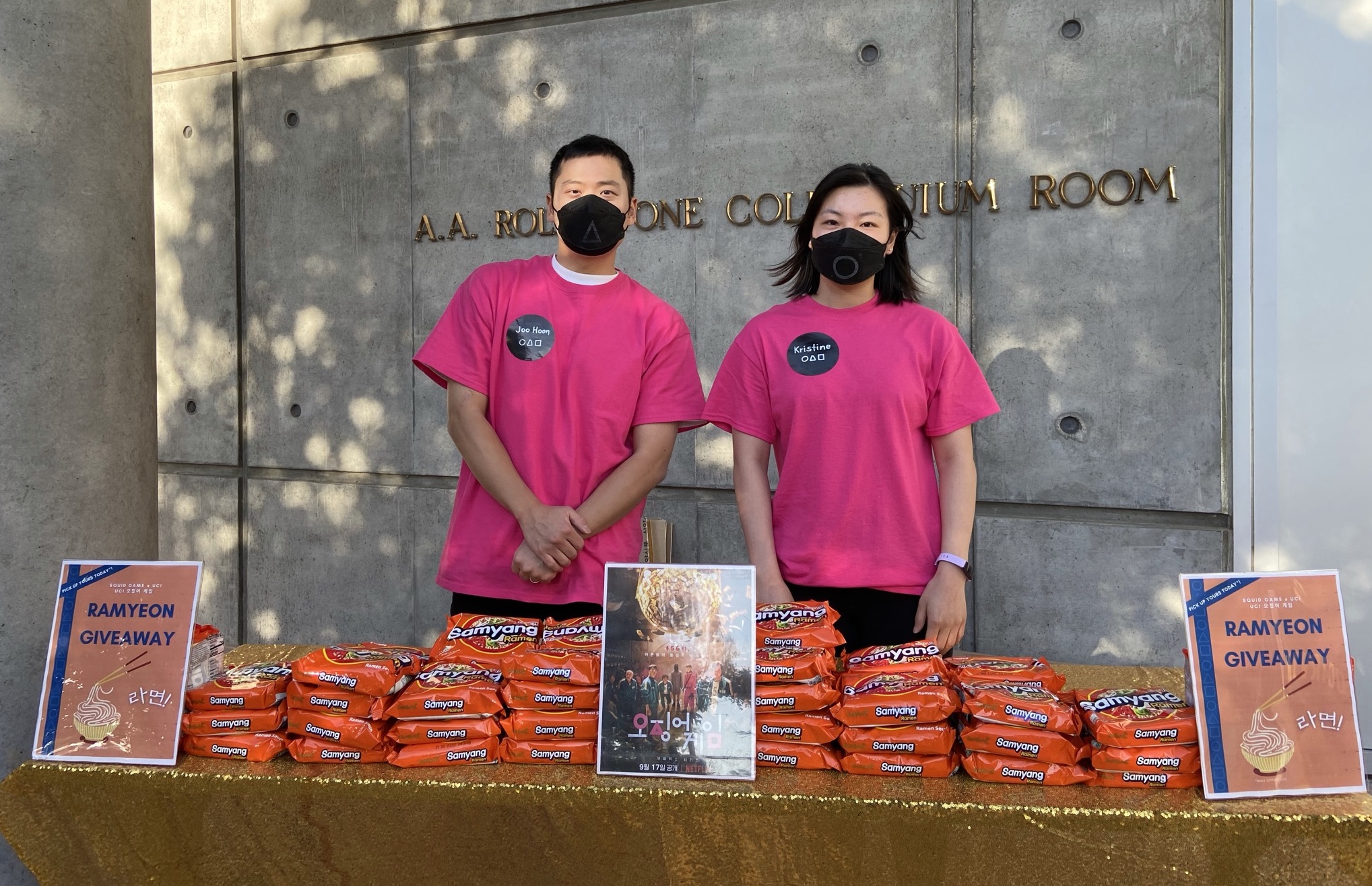 Two students wear hot pink shirts and black face masks, emulating characters in Squid Game
