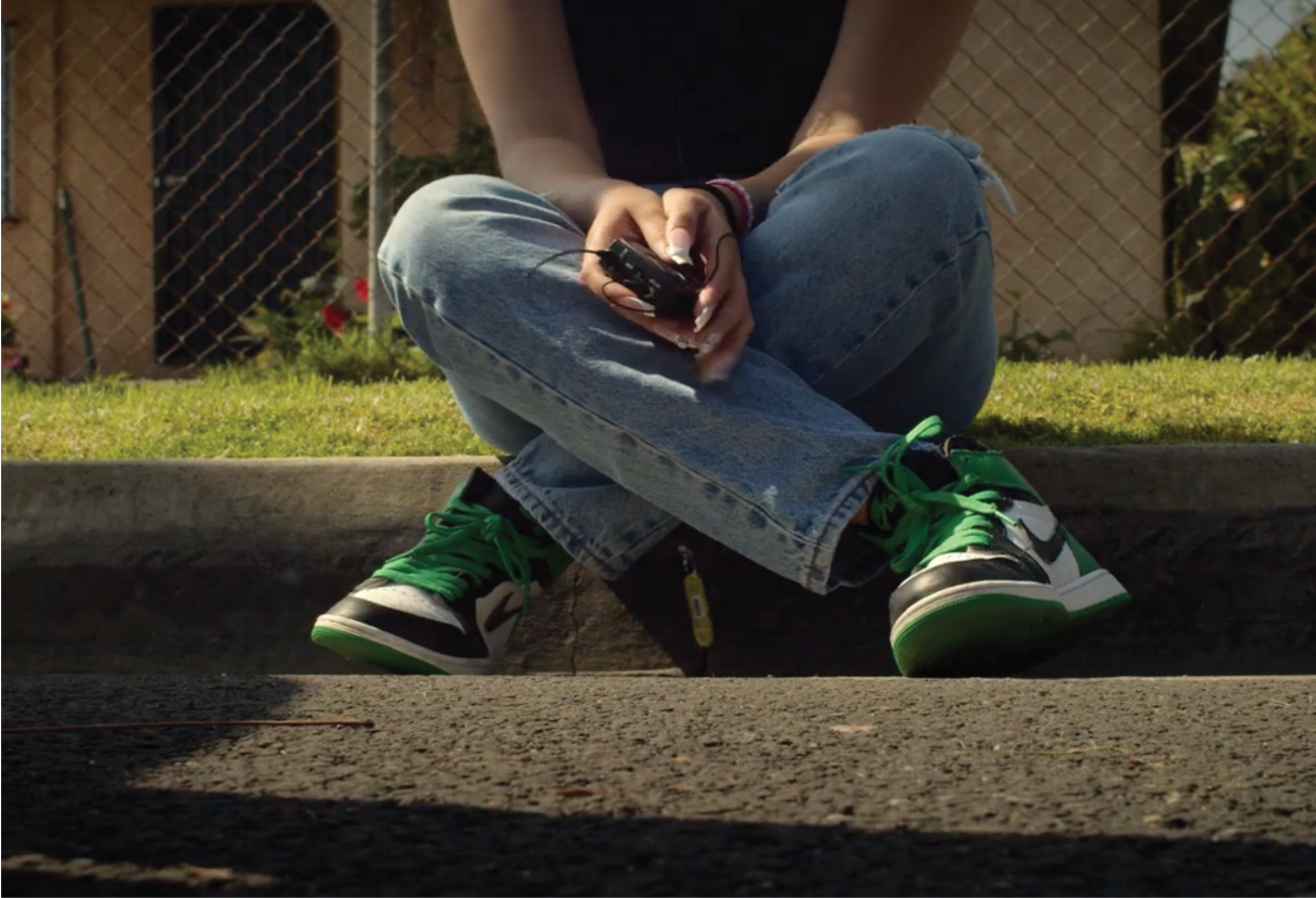 A still from the film Little Angels: A girl in green and white shoes sits on a curb