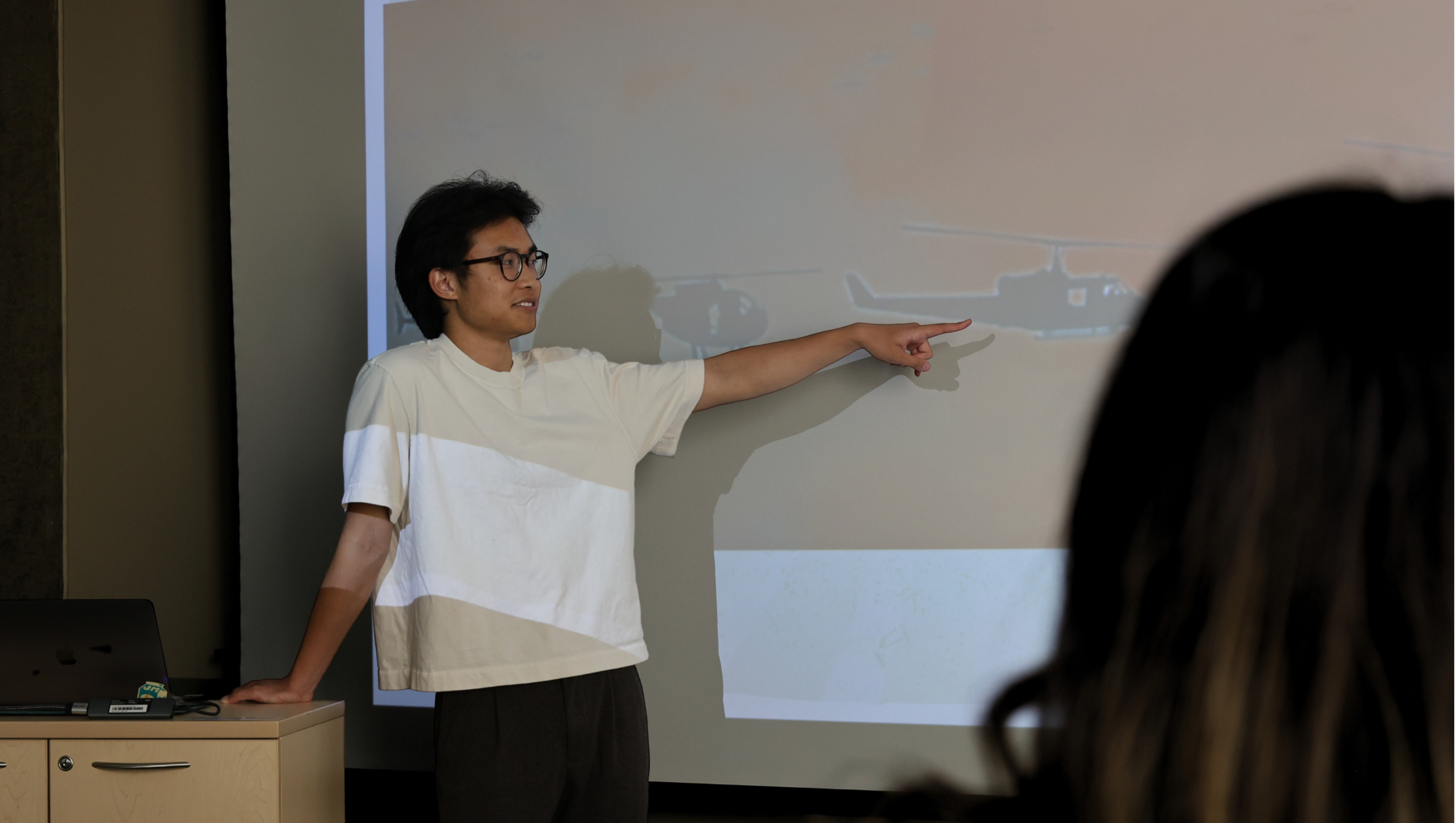 An action shot of UTeach student Brian Nguyen in the classroom talking about his powerpoint slide.