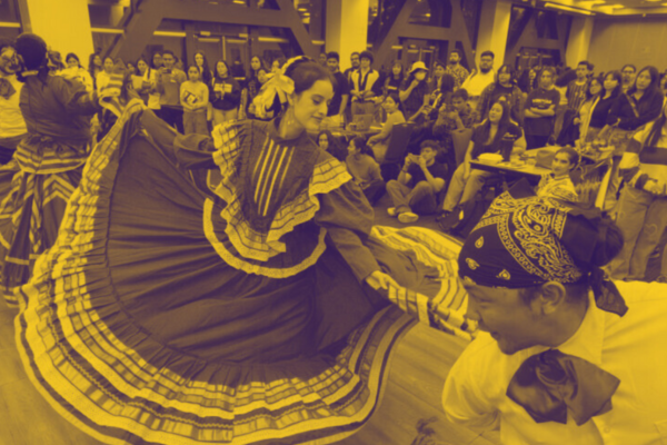 A lively dance performance showcasing a woman in a traditional, colorful dress gracefully twirling. A man dances nearby. A captivated audience watches.