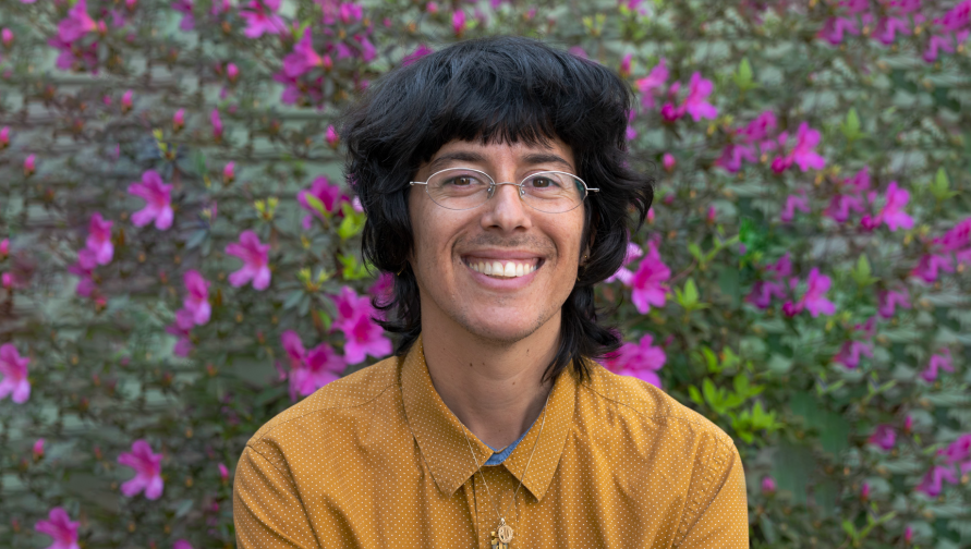 A headshot of Dan Bustillo against a wall covered with magenta flowers