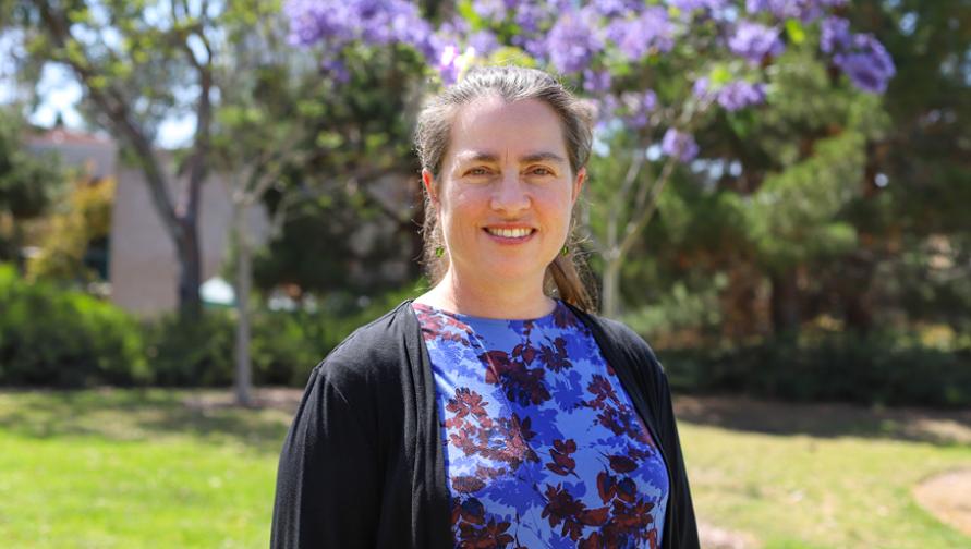 A headshot of Nancy McLoughlin with jacaranda trees in the background