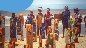 A group of people in traditional African outfits stand on a beach.