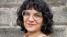 Face of smiling person with dark curly hair and glasses