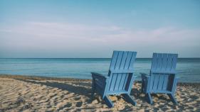 blue Adirondack chairs on sandy beach facing the ocean