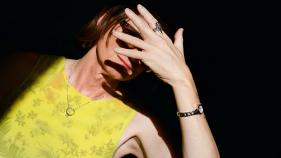 woman against black background with hand covering her face