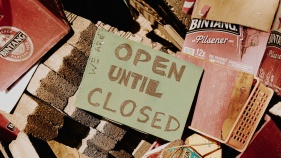 Open Until Closed sign sitting on a pile of bricks and books
