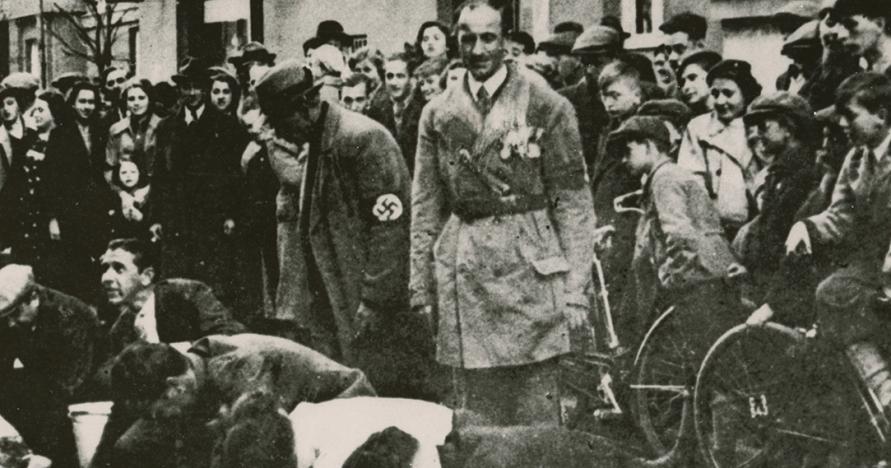 black and white image of Polish Jews scrubbing street overseen by Nazi official