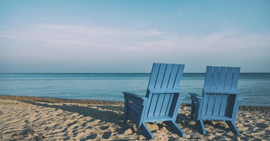 blue Adirondack chairs on sandy beach facing the ocean