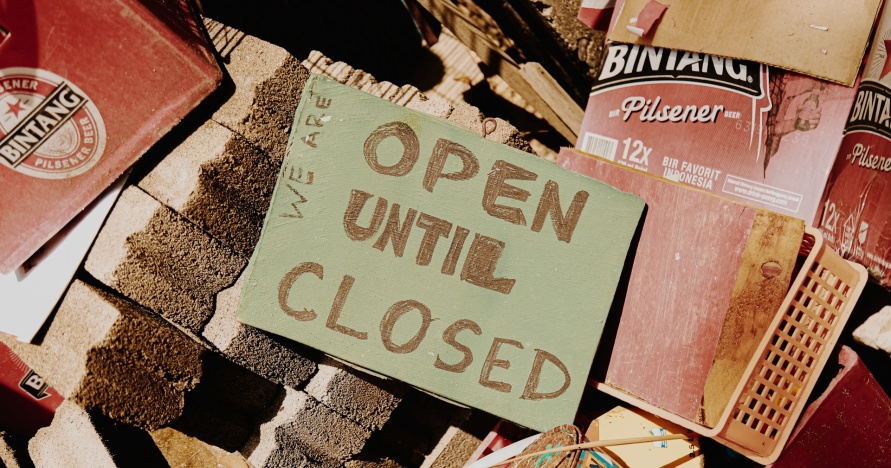 Open Until Closed sign sitting on a pile of bricks and books