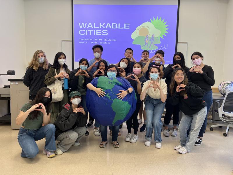 Students standing at the front of a classroom wearing masks, one student is wearing an Earth costume