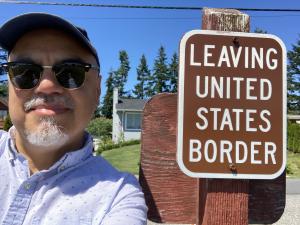Tobar in front of Leaving United State Border sign (Canada)