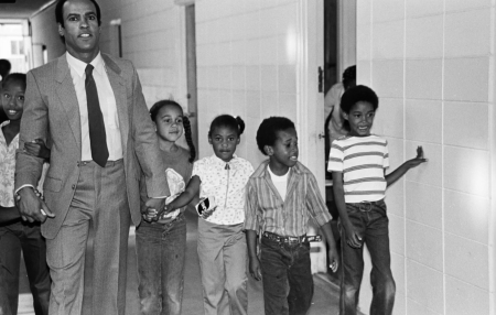 A black and white photo of Huey P. Newton walking alongside students