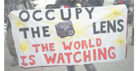 Image of a poster saying "Occupy the lens, the world is watching"