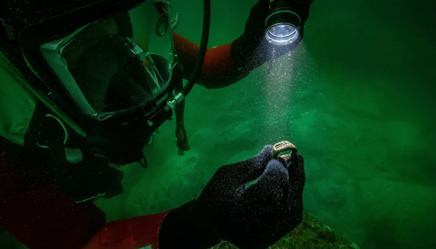 Scuba diver holding up a shining object and looking at it with a flash light.