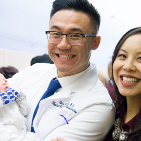 Calvin Ho holding a baby in his doctor attire with a woman behind him