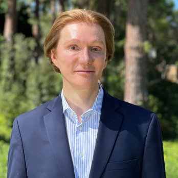 A photo of Gregory Cox, wearing a suite and standing in a park. 