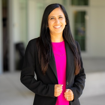 Shabnam Malek-Cazares smiling, wearing a black blazer and pink top.