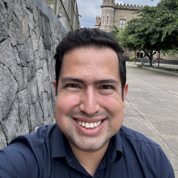 Brunette man who is smiling and wearing a blue shirt in front of a historical building