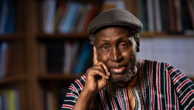 Ngugi rests his head lightly on his left hand; he is in a library