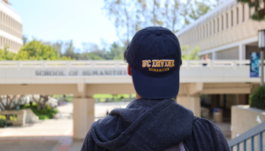 Transfer students Ryan Trang stands in front of the School of Humanities bridge with a School of Humanities backwards baseball hat on.